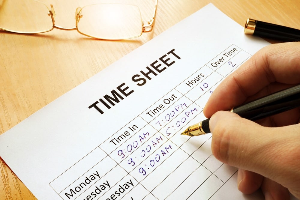 Employee writing hours on paper timecard.